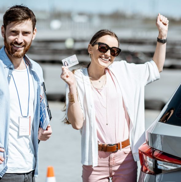 Instructor with happy woman getting a driver's license while standing together on the training ground outdoors